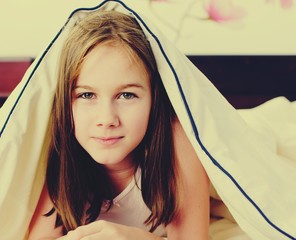 Close up portrait of an white Caucasian young girl (child, kid) covered with blanket in bed. Lifestyle concept. Filter applied. 