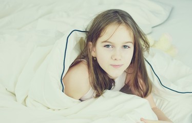 Portrait of an white Caucasian young girl (child, kid) covered in the morning in bed with blanket. Lifestyle concept. Filter applied.