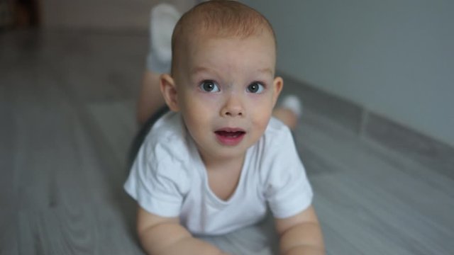 Close portrait. A two-year-old baby lies on the floor on his stomach and waves his legs. Happy childhood, blue-eyed child