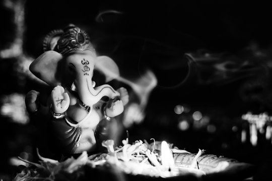black and white photography of lord ganesha statue with earthen lamp against dark background. hinduism and faith concept...