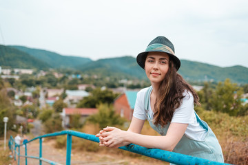 Fototapeta na wymiar Portrait of a young beautiful brunette woman in hat posing near the railing against a rural view