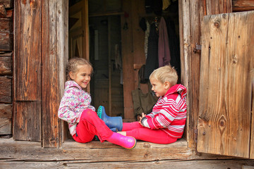 Children having rest on the doorstep of old wooden house during summer vacation, eco-friendly...
