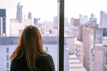 Fototapeta na wymiar 高層ビルの窓から都会の景色を眺める若い女性の後ろ姿