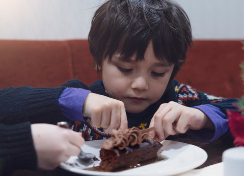Candid shot humgry kids eating chocolate cake in the cafe, Cute little boy emjoy eating dessert for snack time.