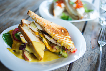 Classic breakfast, hot sandwiches with cheese, vegetables and chicken on a wooden table. Hand-made, rustic breakfast, toast with turkey and vegetables. Soft focus.