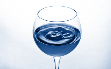 glass goblet on white background with  liquid splashing. Toned trendy classic blue color of year 2020.
