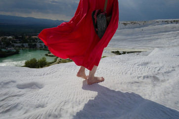 Young barefoot girl in long red dress on white travertines in Pamukkale and looking to wide panoramic landscape. Pamukkale, Tureky.
