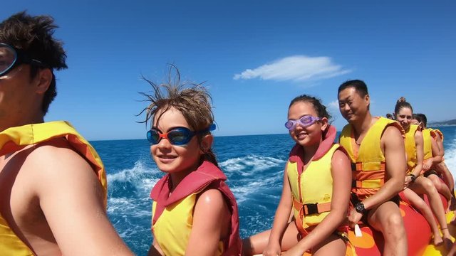 Happy people having fun in the sea on water attractions. Tourists on inflatable banana smiling and waving hands. Family on summer vacation