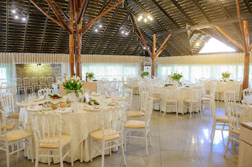 close up photo of a banquet room at a christening party: arranged white round tables with vases with tulips and plates with dishes on it