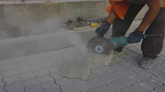 A worker is cutting a stone tile with a grinder, a worker is using a grinder to cut a brick