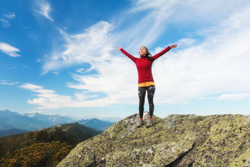The young girl  at the top of the mountain raised her hands up on blue sky background. The woman climbed to the top and enjoyed her success.