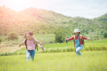 Fototapeta premium Two children carrying a backpack in their backs and wearing a hat, standing under a tree in the countryside. She walked and enjoyed the surrounding nature. She enjoys traveling during the summer.