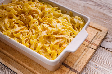 Close up of baked fettuccine with cheese and smoked sausage in a ceramic bowl on a wooden table. Italian pasta