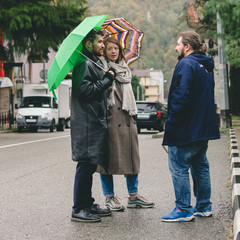 Three friends, a girl with an umbrella and two guys met on the street and talking.