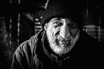 Close up portrait of old smiling homeless alcoholic man face with white beard and hair wandering on...