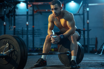 Plakat Caucasian man practicing in weightlifting in gym. Caucasian male sportive model posing before training, looks confident and strong. Body building, healthy lifestyle, movement, activity, action concept