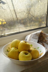 Natural yellow apples in a white plate on a windowsill, organic fruits on a sunny winter day.