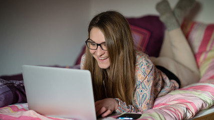 Junge Frau mit Laptop liegt zuhause auf dem Bett und lacht