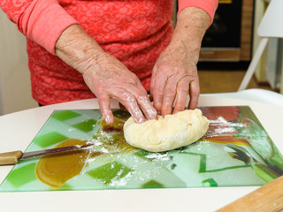 An old woman (80 years old) cooks at home in the kitchen, makes dough, kneads the dough.