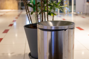 close-up steel cylinder bin litter bin. near in blur a plant in a gray tub. Against the background...