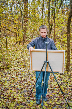 Man painting on canvas in forest