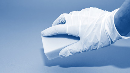 Banner with human hand in white glove holds a white melamine household sponge for cleaning on blue...