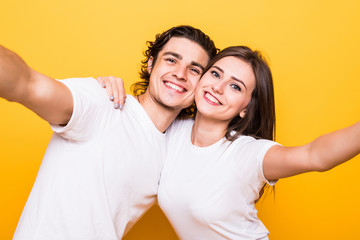 Portrait closeup of joyful man and woman laughing and taking selfie photo isolated over yellow background