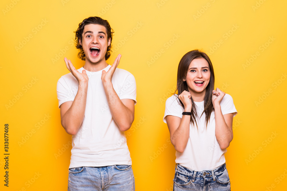 Wall mural excited couple two friends guy girl in white empty blank design t-shirts posing isolated on yellow o