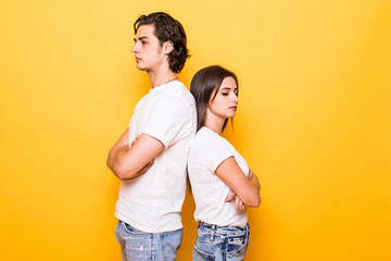 Confused young couple standing with one another's back and looking at the camera with crossed arms over yellow background