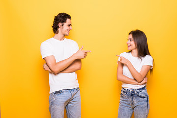 Young people man and woman in basic clothing laughing and pointing fingers at each other isolated over yellow background