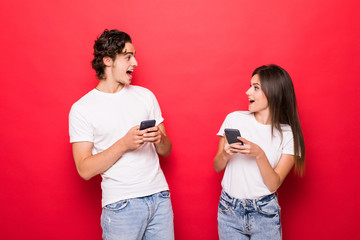 Internet addicted. Two young lovers are busy at their mobile phones in social nets isolated on red background