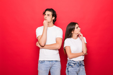 Young couple of friends thinking touching their chins looking up isolated on red background