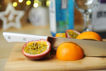 Making cocktail or dessert. Passion fruit and orange on cutting board with knife. Blurry lights in the background.