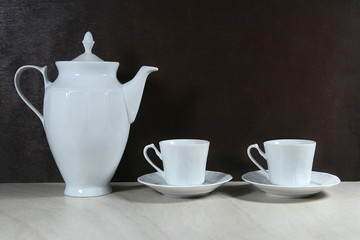 White retro coffee or tea pot with cups on dark background..