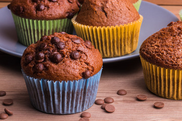 A few chocolate-sprinkled muffins in colored cups on a wooden table.