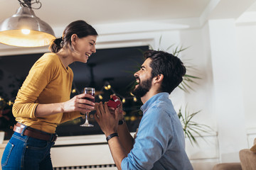 Happy man giving engagement ring in little red box to woman at home