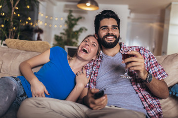 Happy young couple relaxing and watching TV at home.