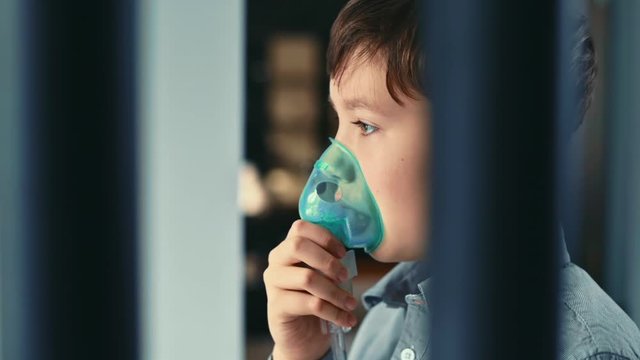 Treatment for asthma, the boy breathes through an inhaler. Standing in the kitchen