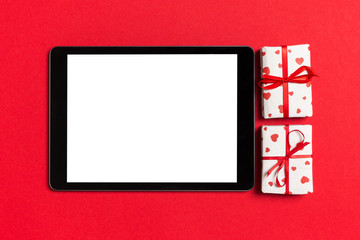 Top view of digital tablet surrounded with gift boxes on colorful background. Saint Valentine's day