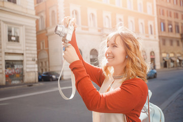 Happy young woman traveler photographer holds camera on European street and takes picture. Summer sun light