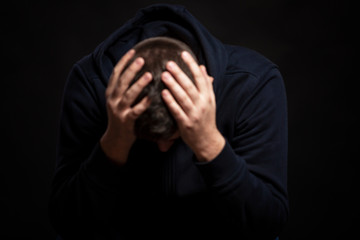 A man is sitting with his head in his hands. Depression and hopelessness. Blurred. Black background. Close-up.