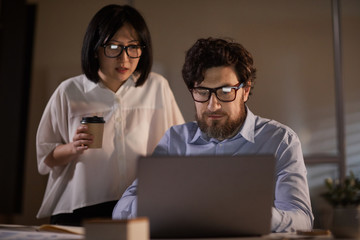 Young business people looking at monitor of laptop and working in team till late at office