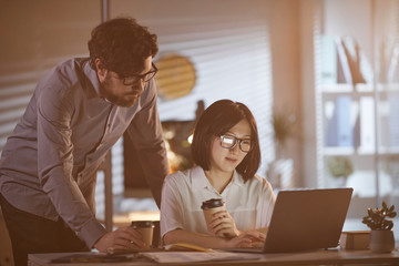 Two business partners drinking coffee and looking at monitor of laptop while working together at office