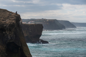 Fototapeta na wymiar Fishermen fishing in Praia de Aljezur beach sea cliff edge, in Portugal