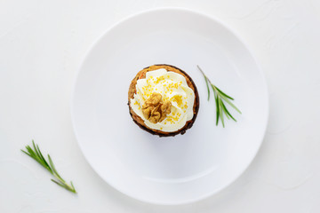 Cupcake with cream cheese, walnut and rosemary on a white plate. Close-up, top view.