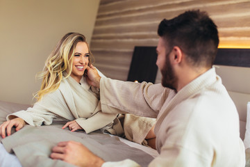Couple in bathrobes lying on bed in hotel room.