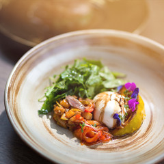 Enjoy the taste. Close up shot of a salad with burrata cheese, tomatoes and arugula dressed with olive oil, in stylish plate. Healthy, summer food concept. Copy space in upper part