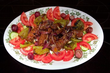Appetizer of roasted sausage, tomato and pepper salad in a white dish isolated on black background. Closeup, soft focus at the background