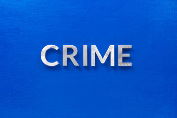 the word crime laid with silver metal characters on blue board in flat lay centered composition