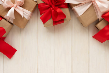 Border from gift boxes wrapped on brown craft paper and red and pink ribbons on white wooden...